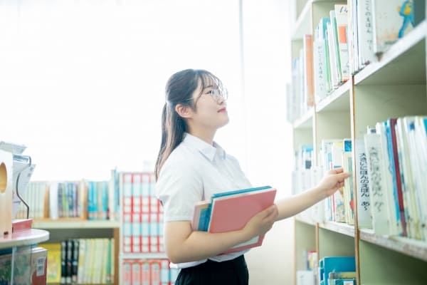 本をもって本棚を見る学校司書の写真